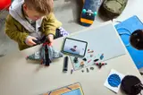 Boy building LEGO Quinjet with digital instructions on tablet.