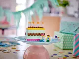 LEGO birthday cake on stand in party setting.