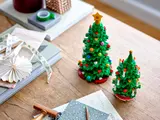 Two LEGO Christmas trees on a table with gift supplies.