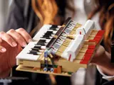 Hands holding LEGO piano keyboard assembly.