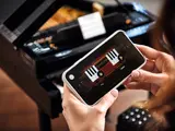 Hands with phone showing LEGO piano play interface.