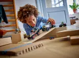 Child playing with LEGO police SUV and criminal truck on a ramp.