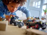Child playing with LEGO police SUV chasing criminal truck, rock trap visible.
