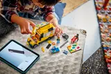 Child building LEGO van with parts and tablet.